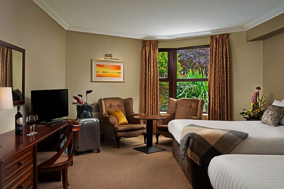 A hotel room with a bed, a desk, a chair, a TV, and a window with curtains.