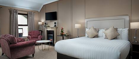 Ein Hotelzimmer mit einem großen Bett, zwei Sesseln, einem kleinen Tisch, einem Kamin und einem an der Wand befestigten Fernseher.