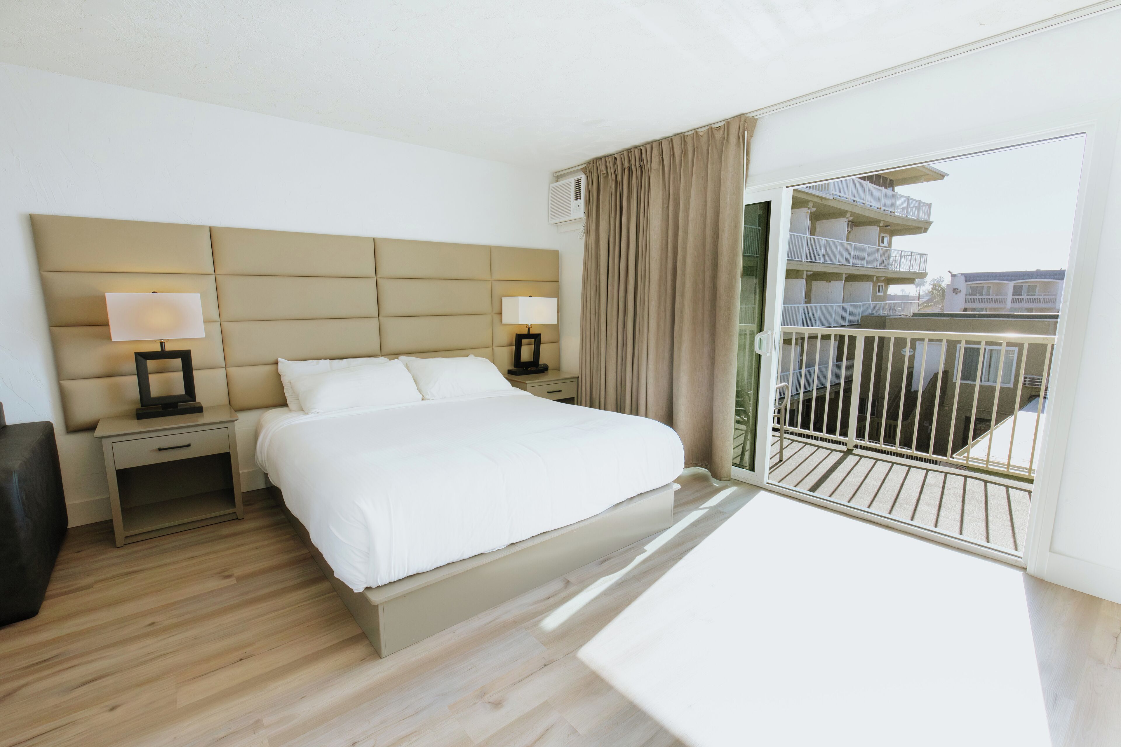 Ein Hotelzimmer mit einem großen Bett, zwei Nachttischen mit Lampen und Balkonblick, im modernen Stil.