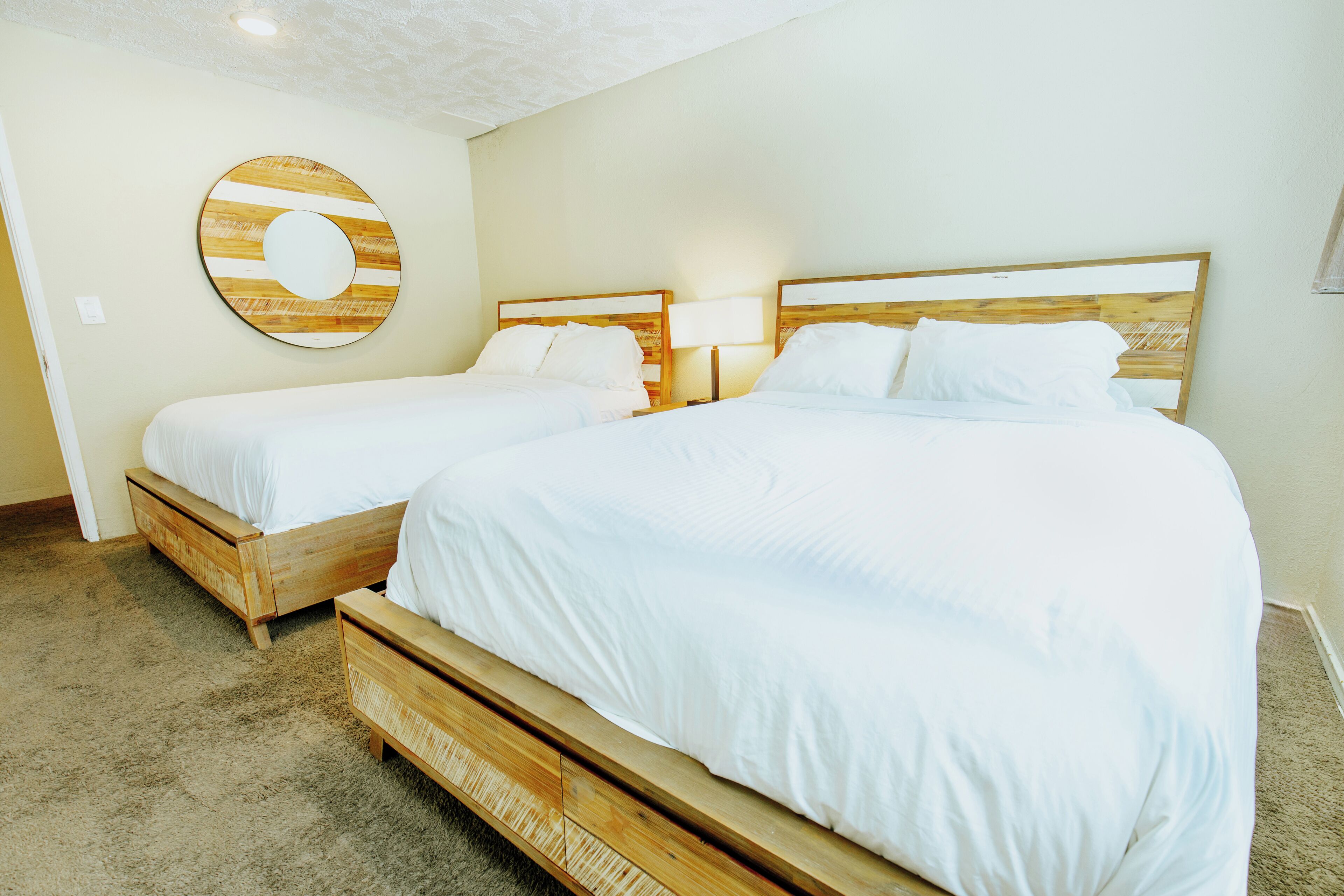 A hotel room with two beds, a wooden headboard, a round wall decoration, and a carpeted floor.