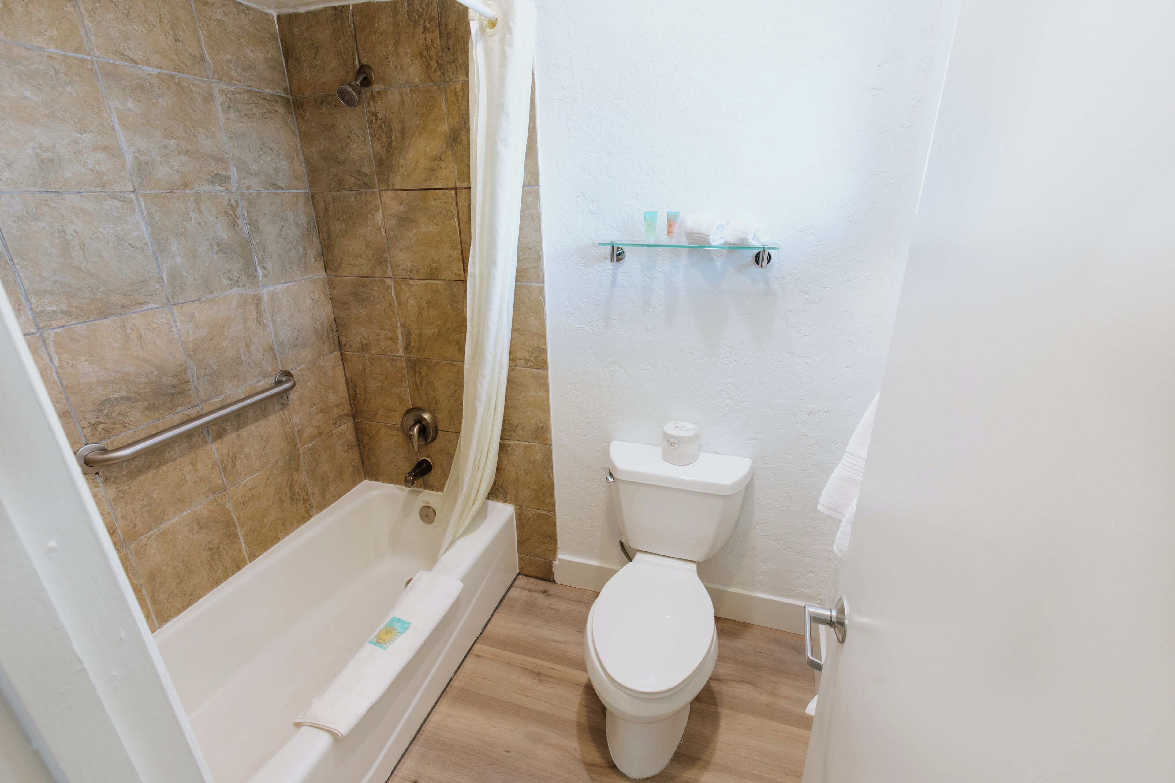 A bathroom with a bathtub, shower, toilet, and a shelf with toiletries.