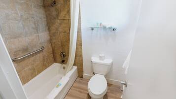 A bathroom with a bathtub, shower, toilet, and a shelf with toiletries.