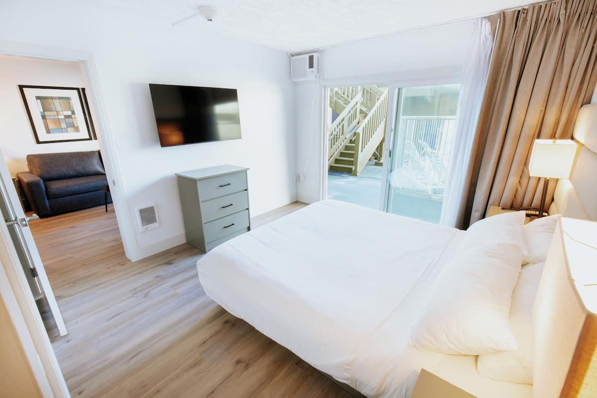 A modern hotel room with a large bed, a flat-screen TV, a desk, and a balcony with a view.