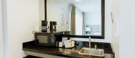 Cocina compacta equipada con microondas, cafetera y pileta.