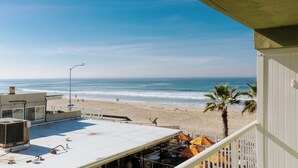 A beach view from a balcony with a white railing, a palm tree, and a sandy beach in the background. - Surfer Beach Hotel (San Diego)