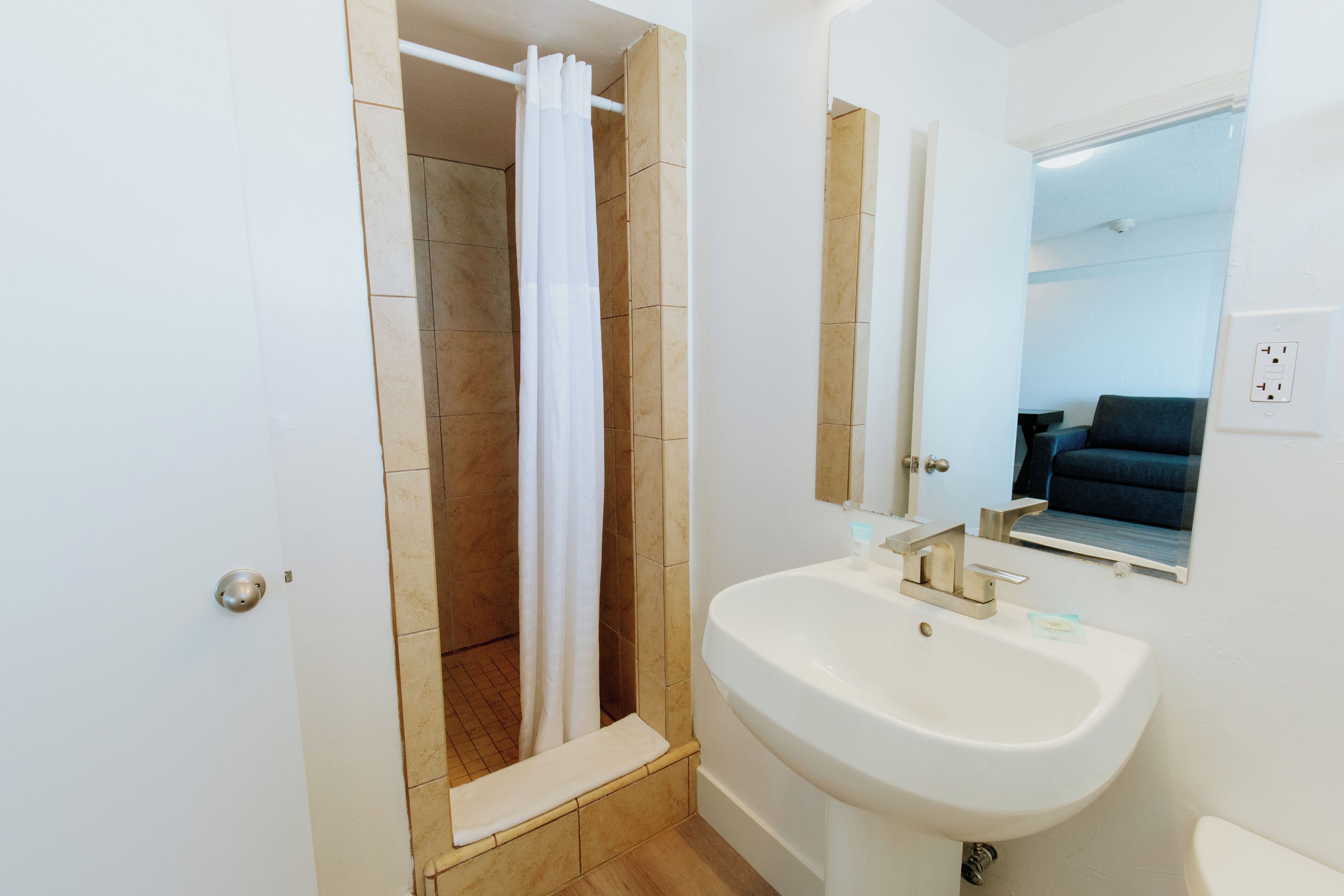 A bathroom with a white sink, a shower with a white curtain, and a mirror above the sink.