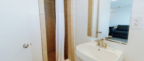 A bathroom with a white sink, a shower with a white curtain, and a mirror above the sink.