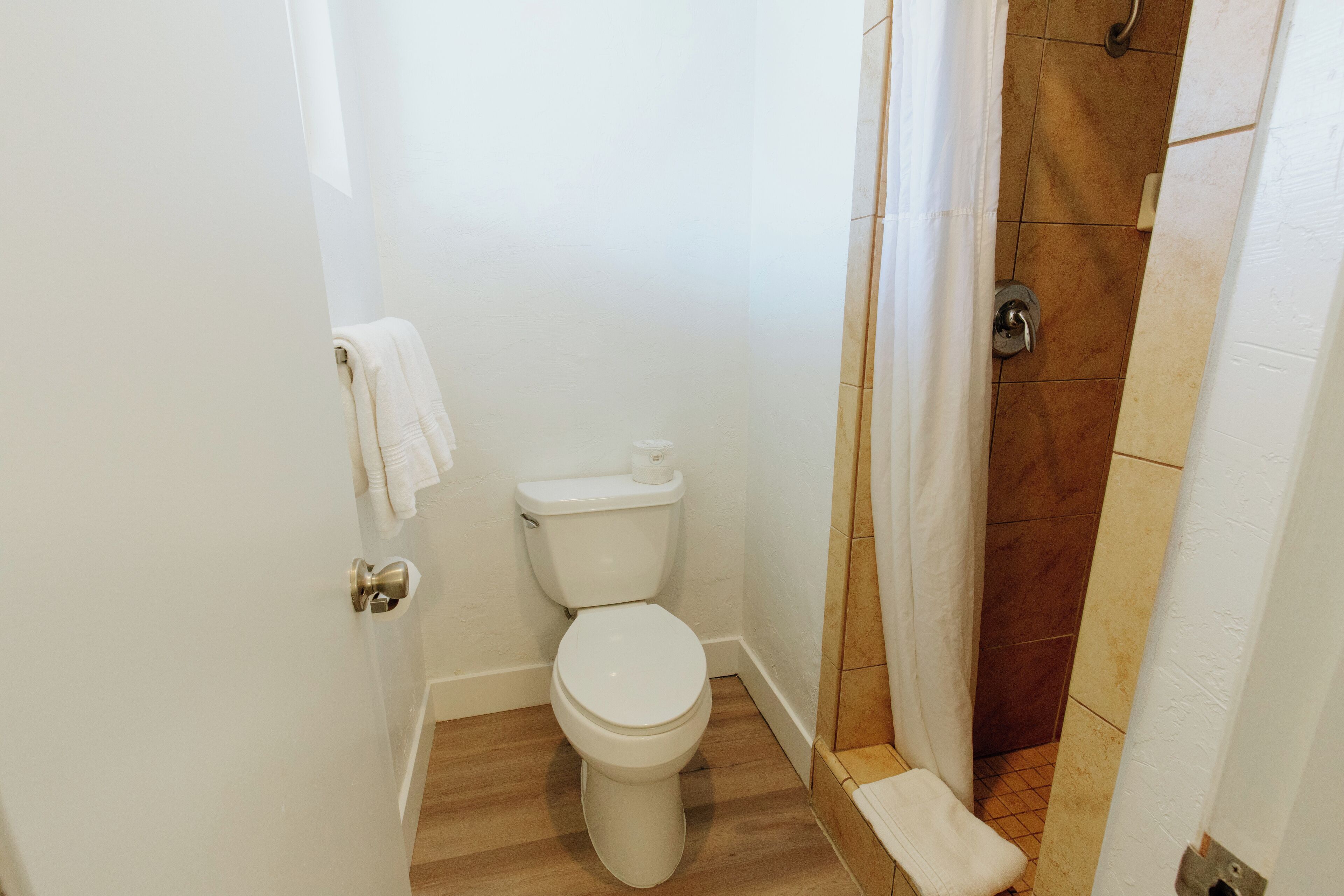 A small, clean bathroom with a toilet, a shower area, and a wooden floor.