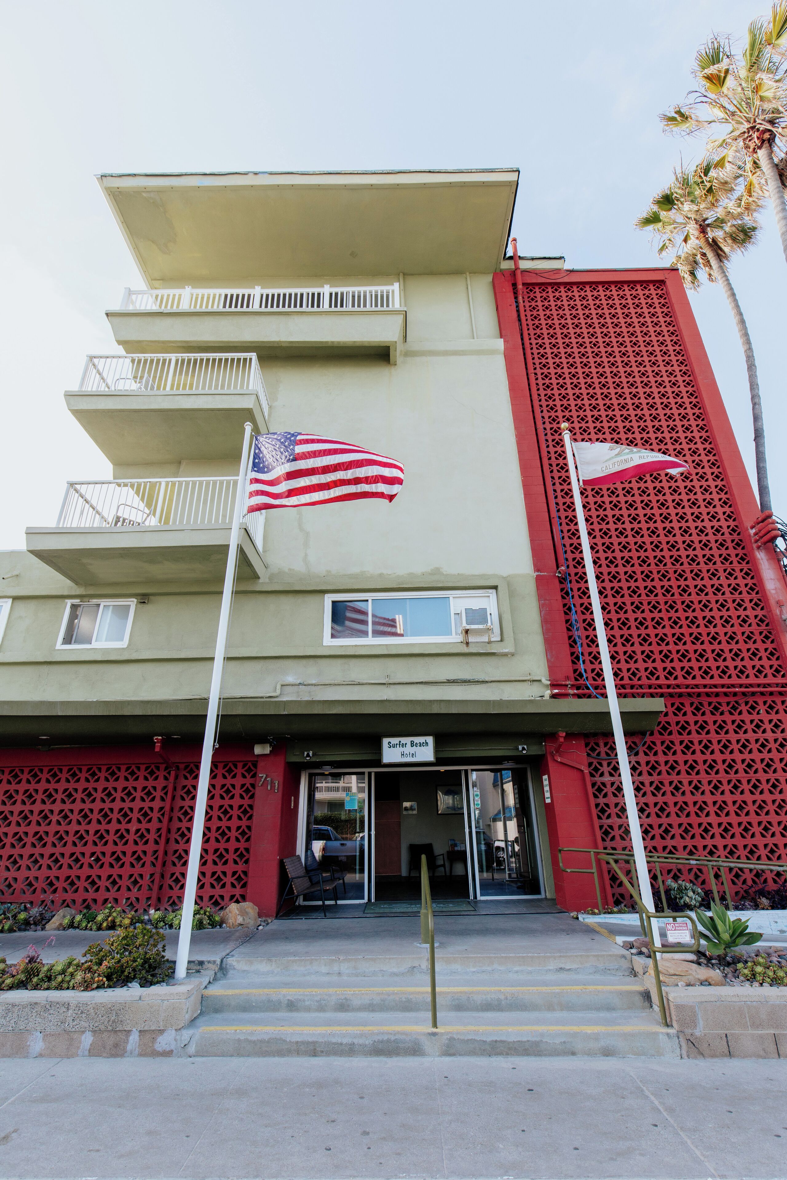A hotel entrance with a flag, a sign, and a red decorative fence.