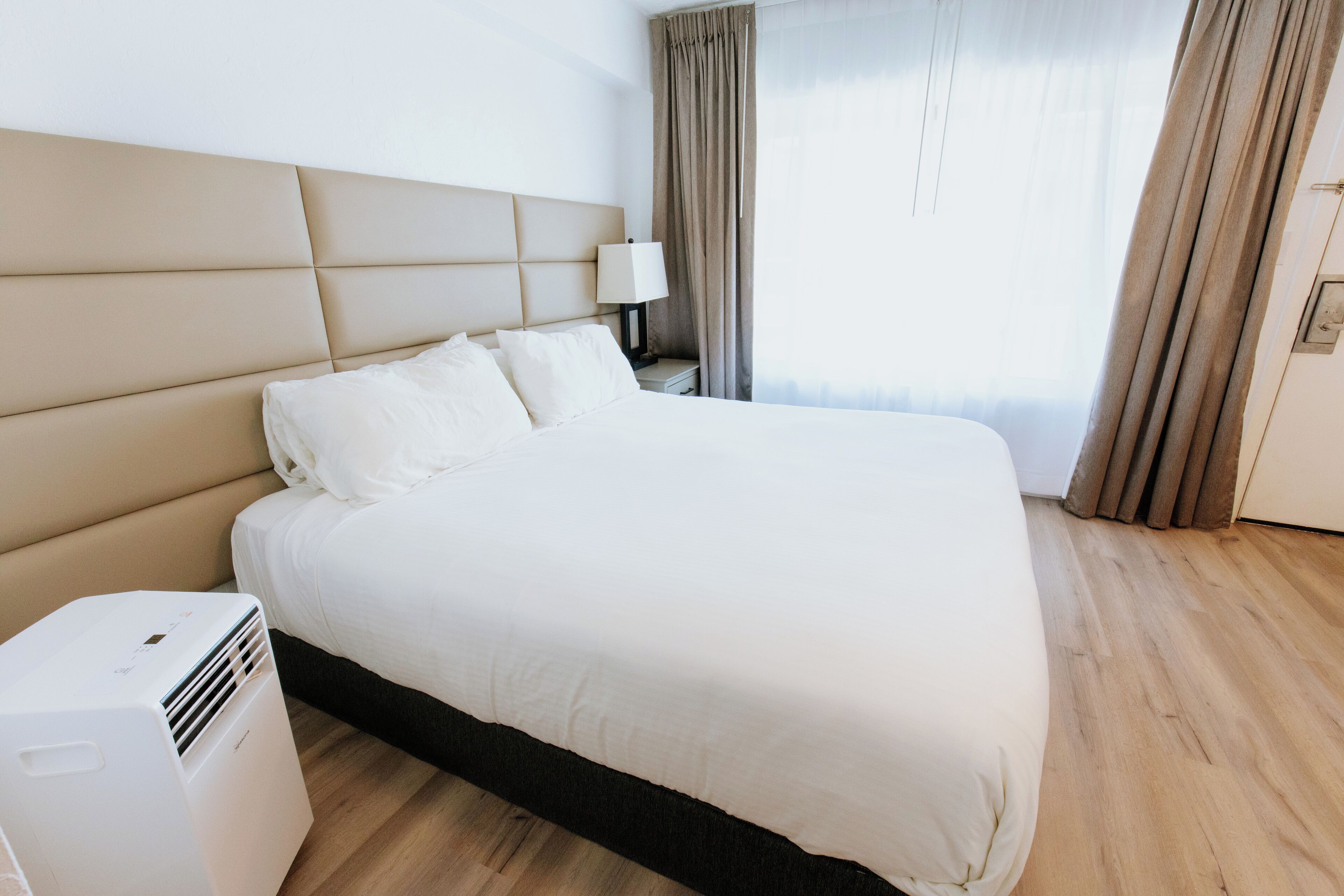 A hotel room with a large bed, a bedside table with a lamp, and a wall-mounted air conditioner.