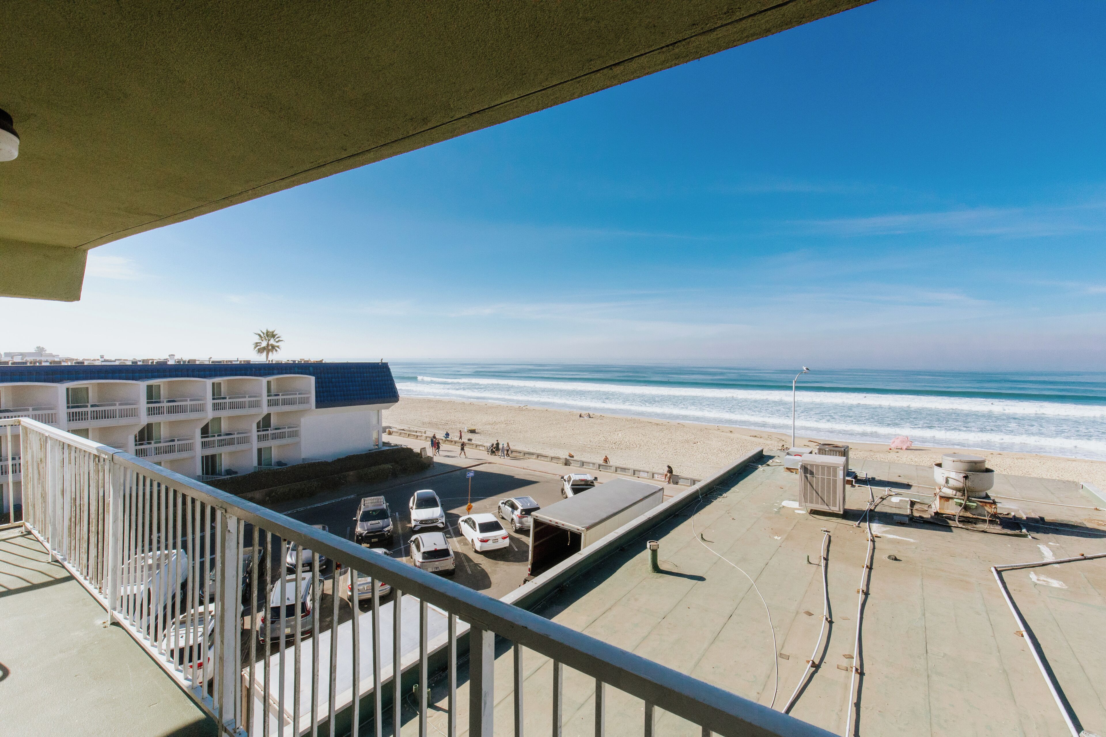 Un balcon avec vue sur la plage, un espace de stationnement et un immeuble doté de plusieurs balcons.