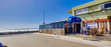 A beachfront restaurant with a clear view of the ocean, a blue awning, and a sign advertising seafood specials.