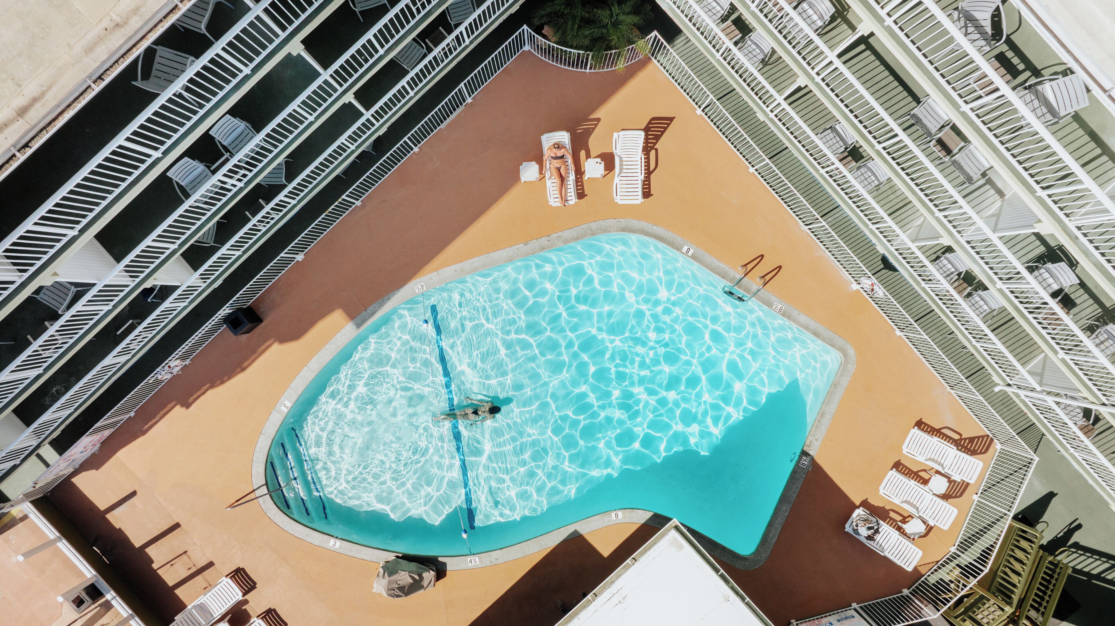 An aerial view of a pool area with sun loungers, a diving board, and a lifeguard stand.