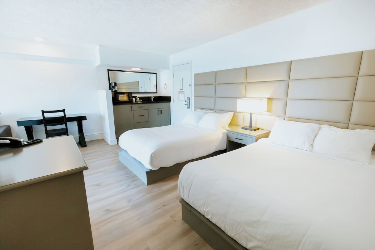 A hotel room with two beds, a desk, a chair, a small kitchenette, and a bathroom.