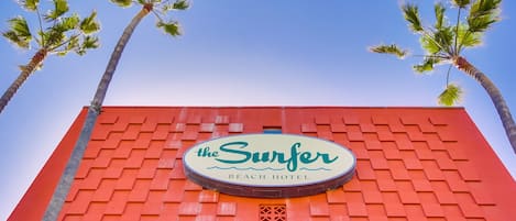 The exterior of the Surfer Beach Hotel with a red facade and palm trees.