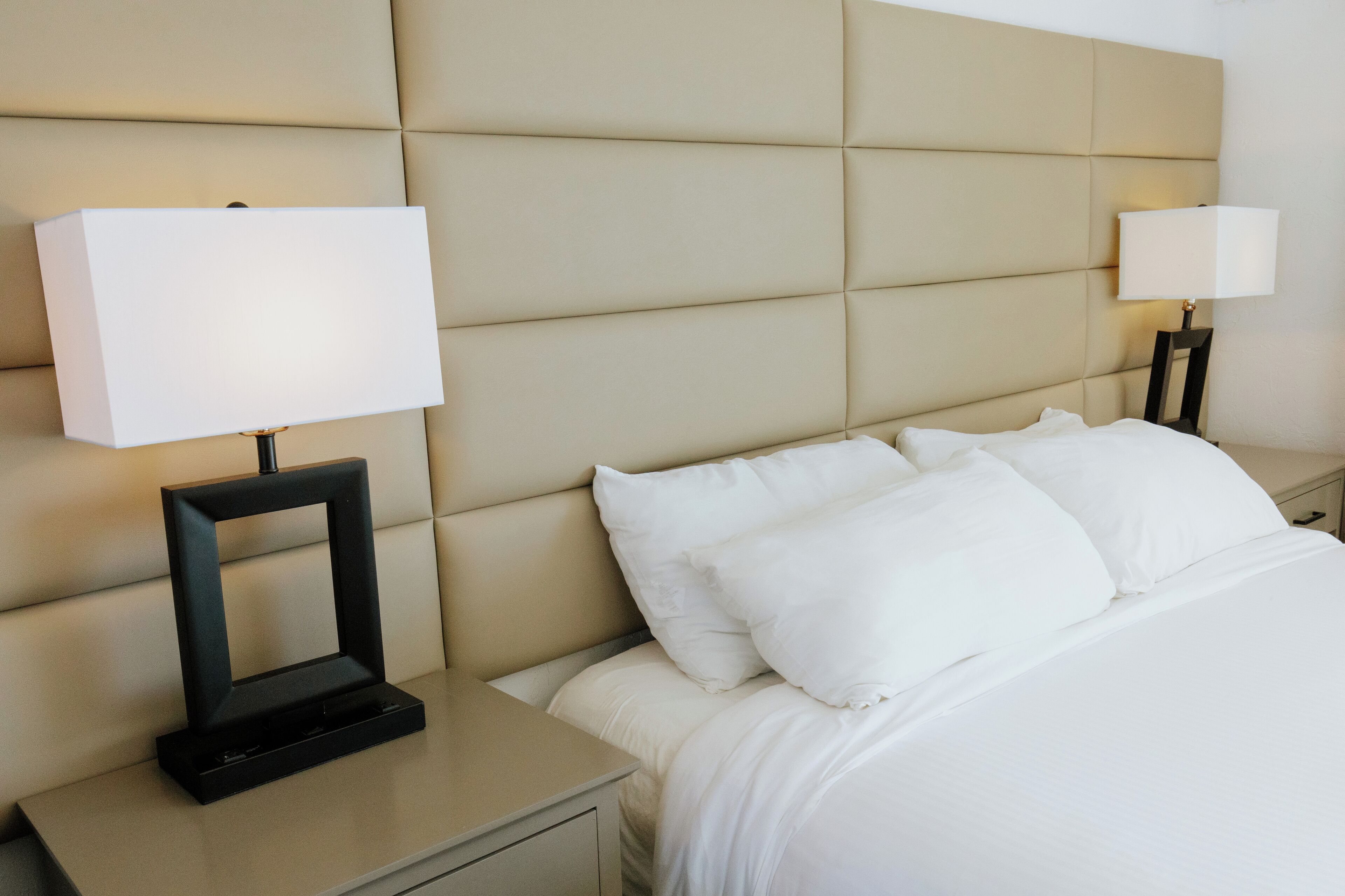 Ein Hotelzimmer mit einem großen Bett, zwei Nachttischen mit Lampen und einem gepolsterten Kopfteil.