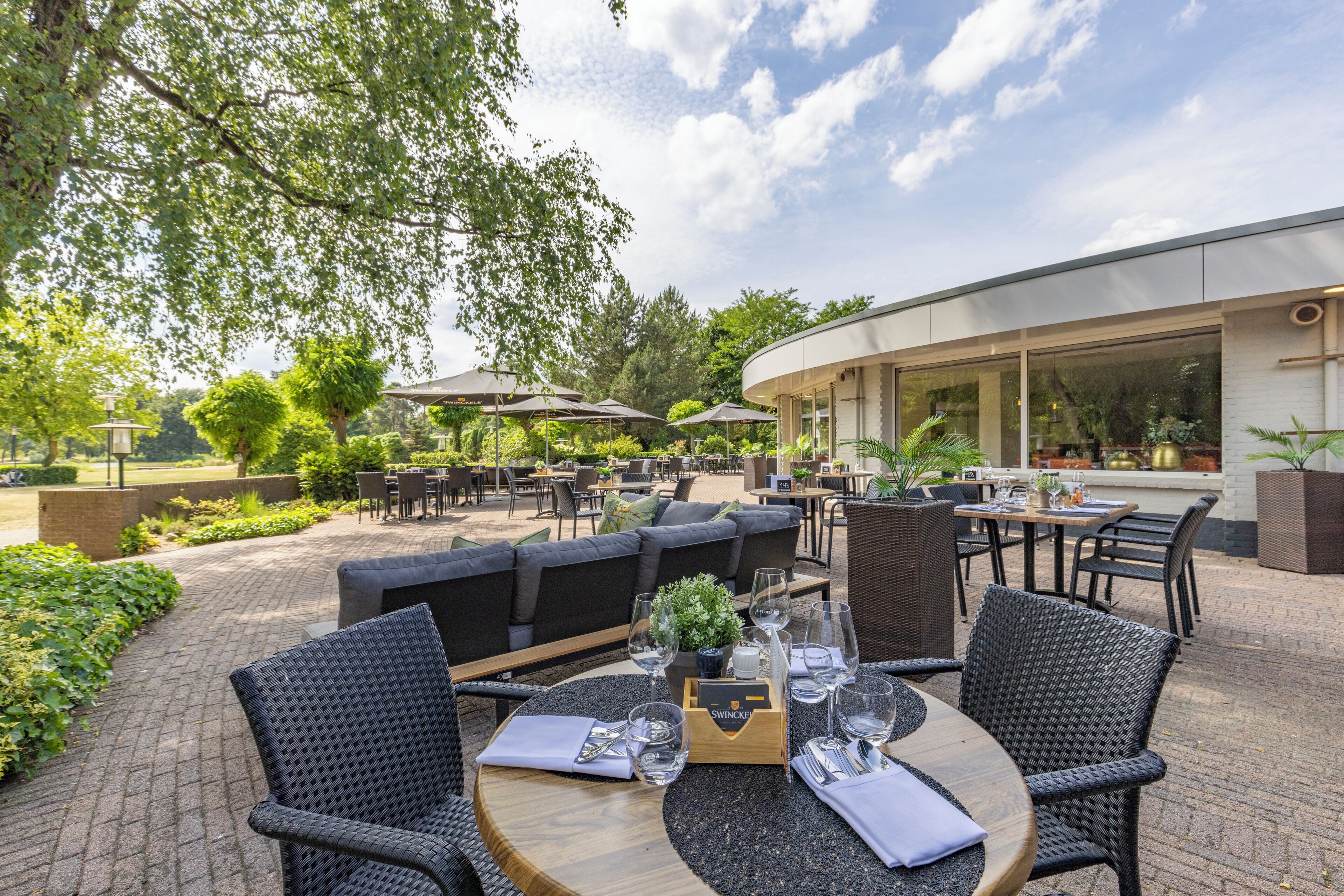 An outdoor dining area with round tables, wicker chairs, and umbrellas.