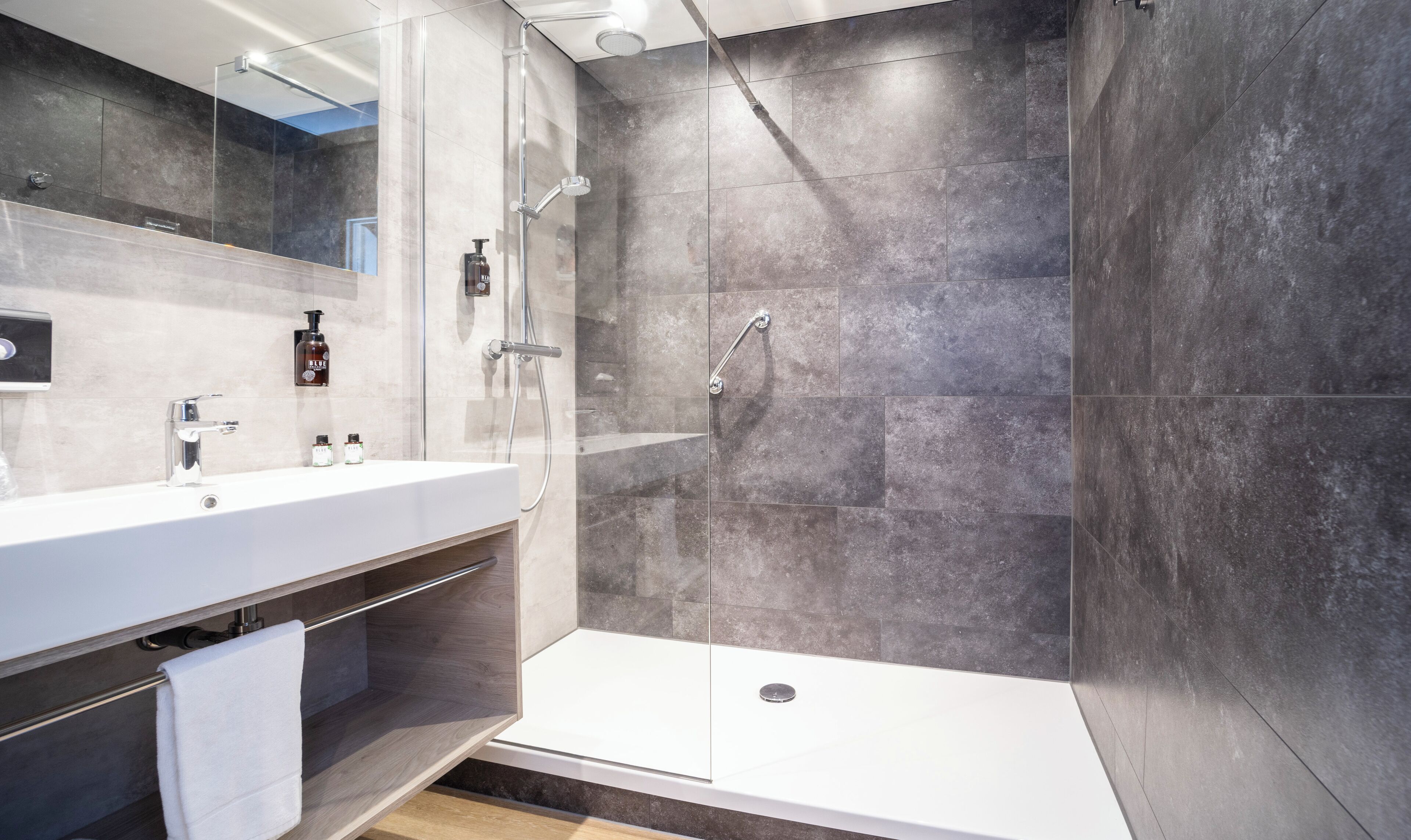 A modern bathroom with a glass-enclosed shower, a white sink, and a mirror.