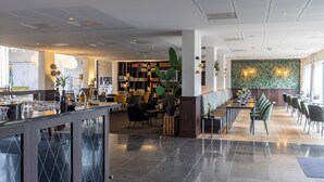 Un hall d’hôtel moderne doté d’un bar, de coins salon et d’une grande bibliothèque.