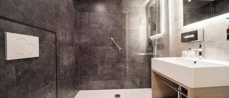 A modern bathroom with a walk-in shower, a large mirror, and a vanity with a sink.