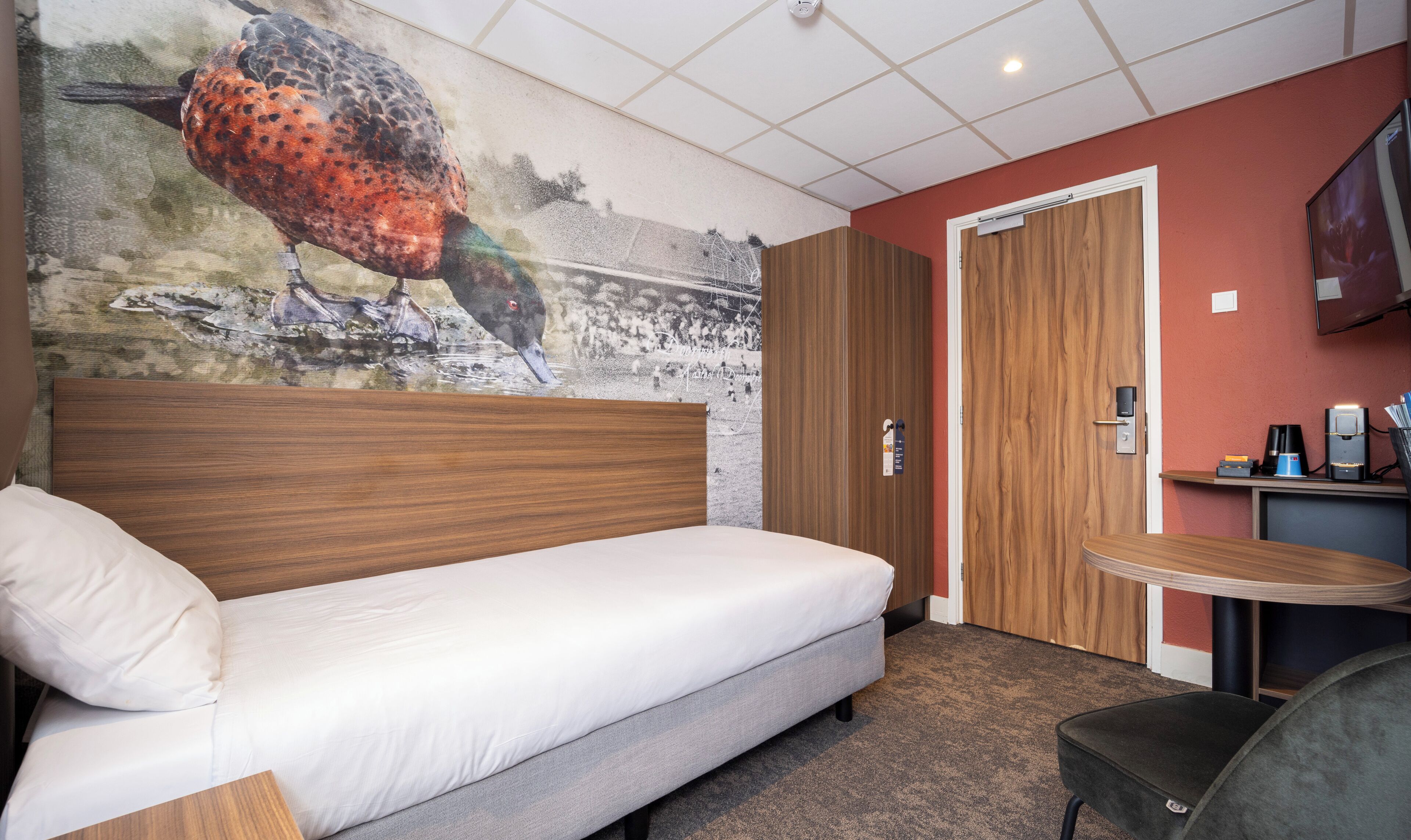 Habitación de hotel con cama, escritorio con silla, armario de madera y un mural en la pared.