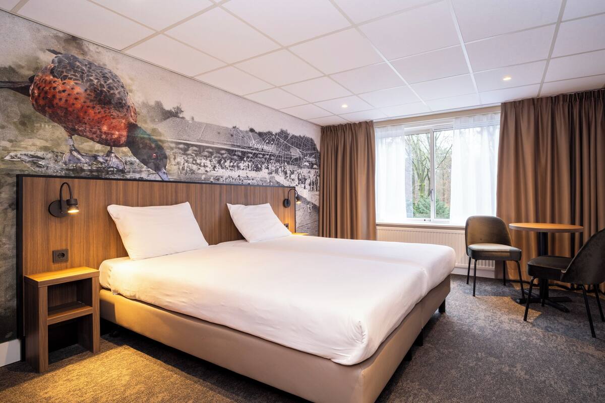 Ein Hotelzimmer mit einem großen Bett, einem Schreibtisch, einem Sessel, einem Fernseher und einem Wandgemälde.
