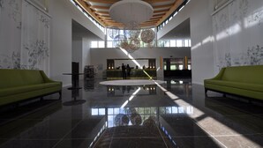 Un hall d’entrée spacieux avec un plafond haut, un comptoir d’accueil central et deux canapés verts.