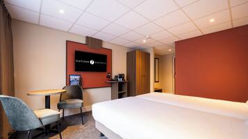 Quarto de hotel com cama, escrivaninha, cadeira, televisão e máquina de café.