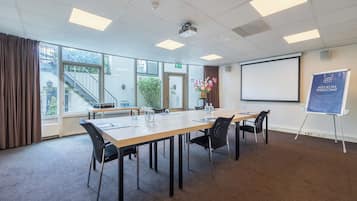 A conference room with a long table, chairs, a projector screen, and a welcome banner.