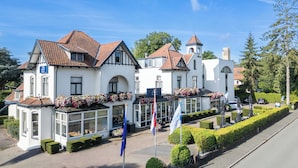 Un edificio de estilo europeo tradicional con una torre destacada, múltiples ventanas y jardineras en el techo.