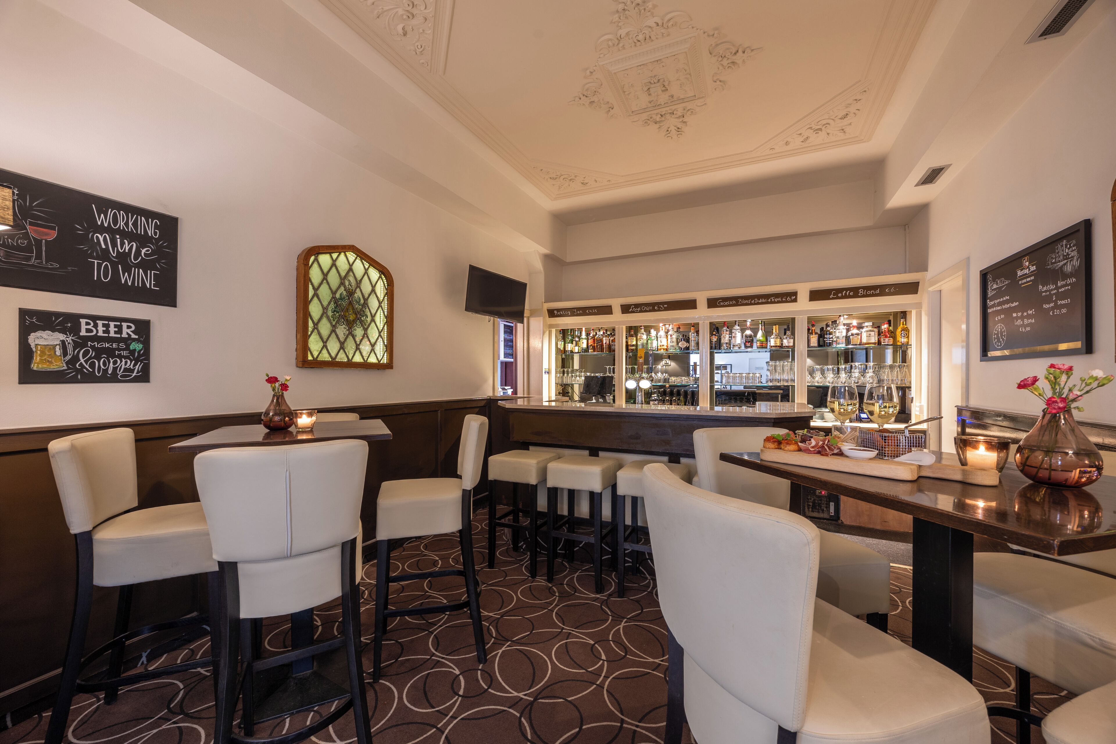 A bar area with high stools, a bar counter, and a wine cooler in the background.