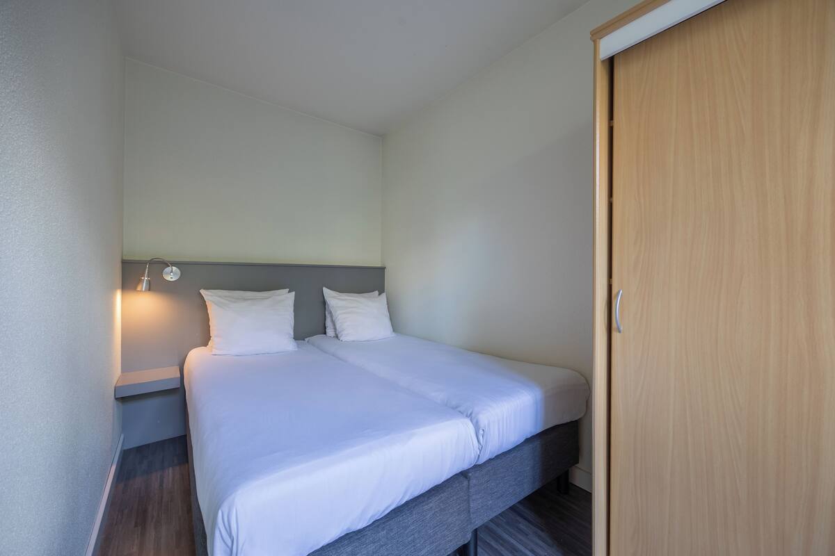 Una habitación de hotel con una cama, una mesita de noche, una lámpara y un armario de madera.
