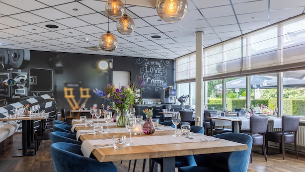 Un restaurante con varias mesas, sillas tapizadas en azul y lámparas colgantes.