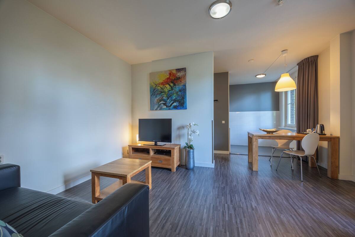 Una sala de estar moderna con un sofá, televisión, una mesa de centro de madera y una zona de comedor con una mesa y sillas.