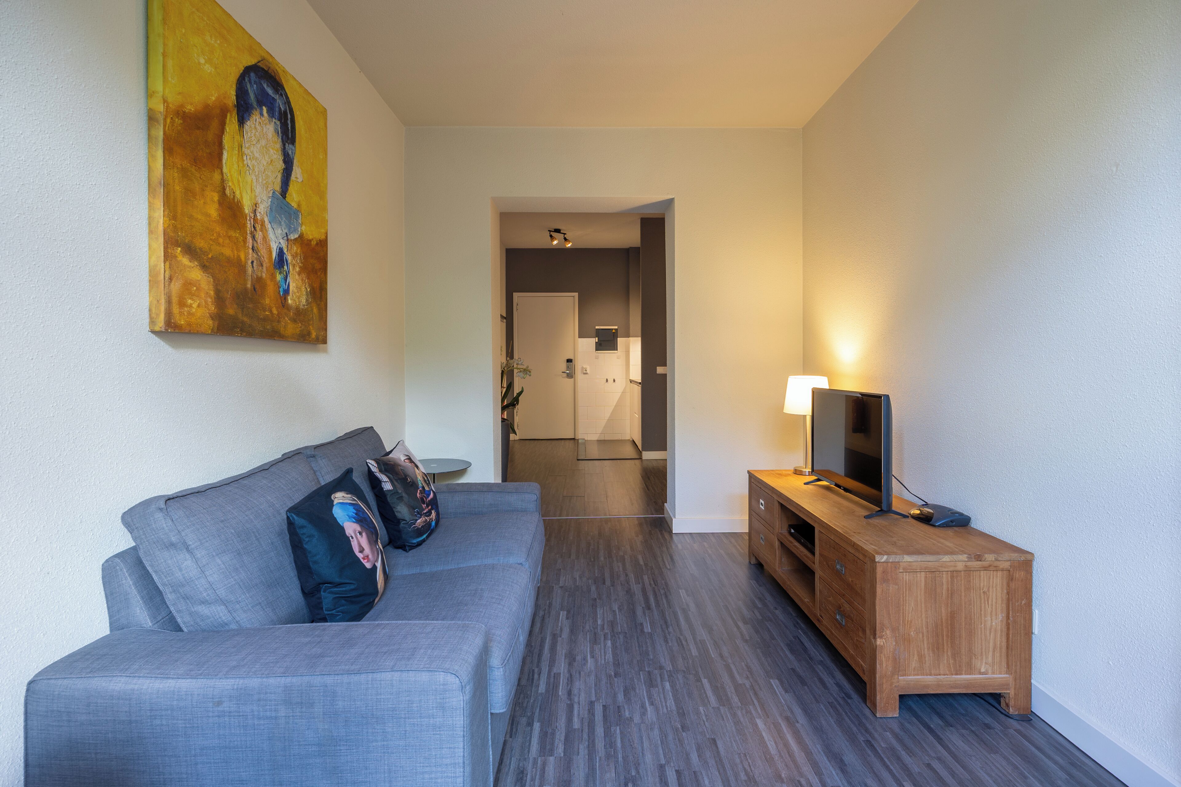 Una sala de estar moderna con un sofá gris, un mueble bajo para televisión de madera y un cuadro en la pared.