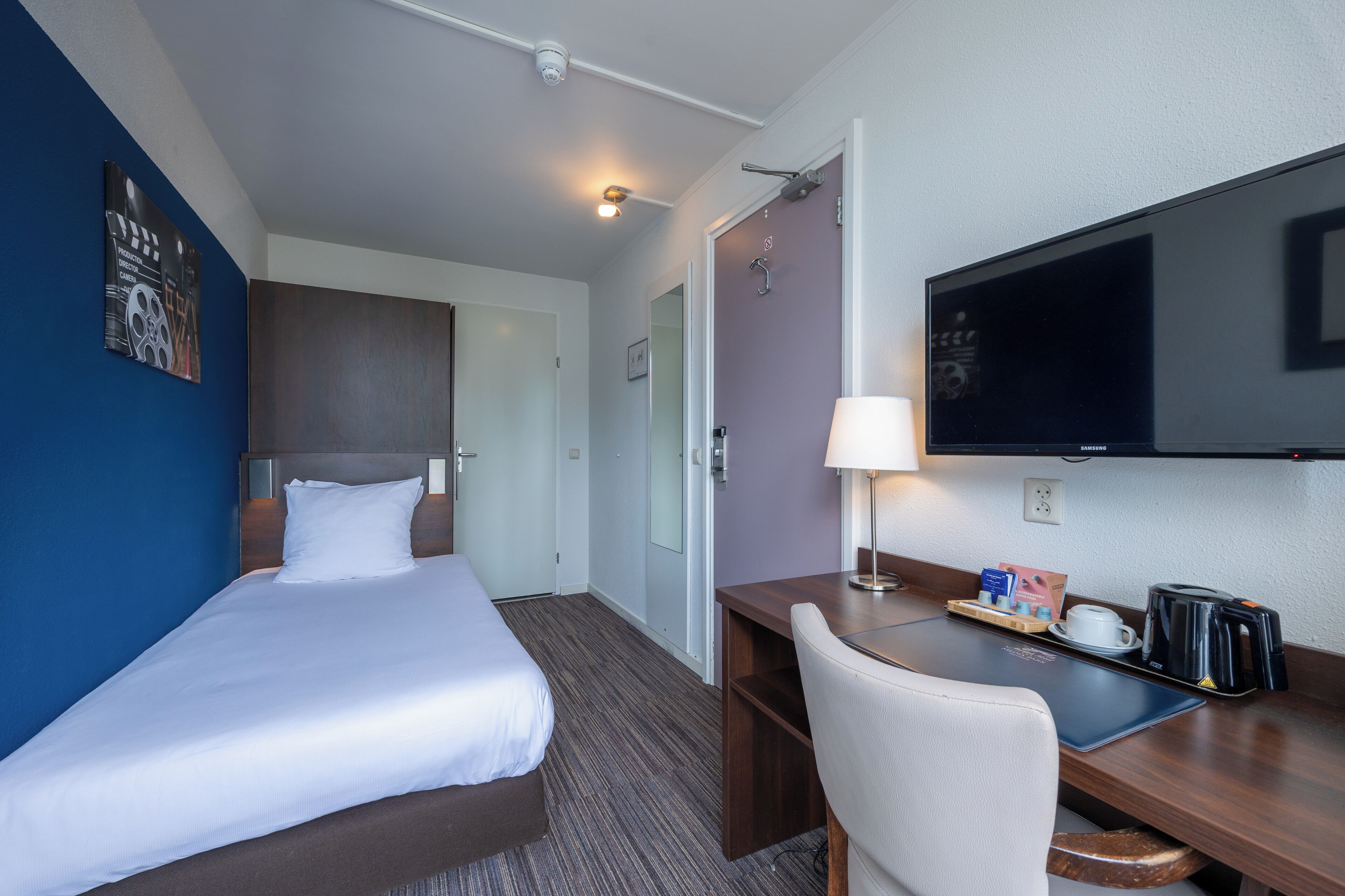 Habitación de hotel con cama, escritorio, silla, televisor y cafetera.