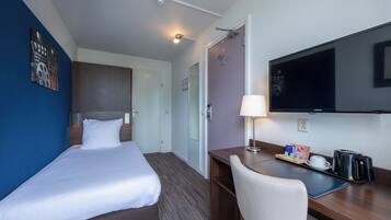 Habitación de hotel con cama, escritorio, silla, televisor y cafetera.