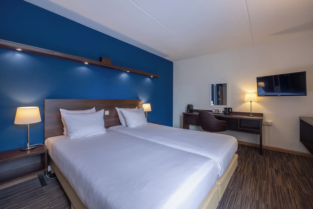 Habitación de hotel con una cama grande, un escritorio con silla, televisión y lámpara.