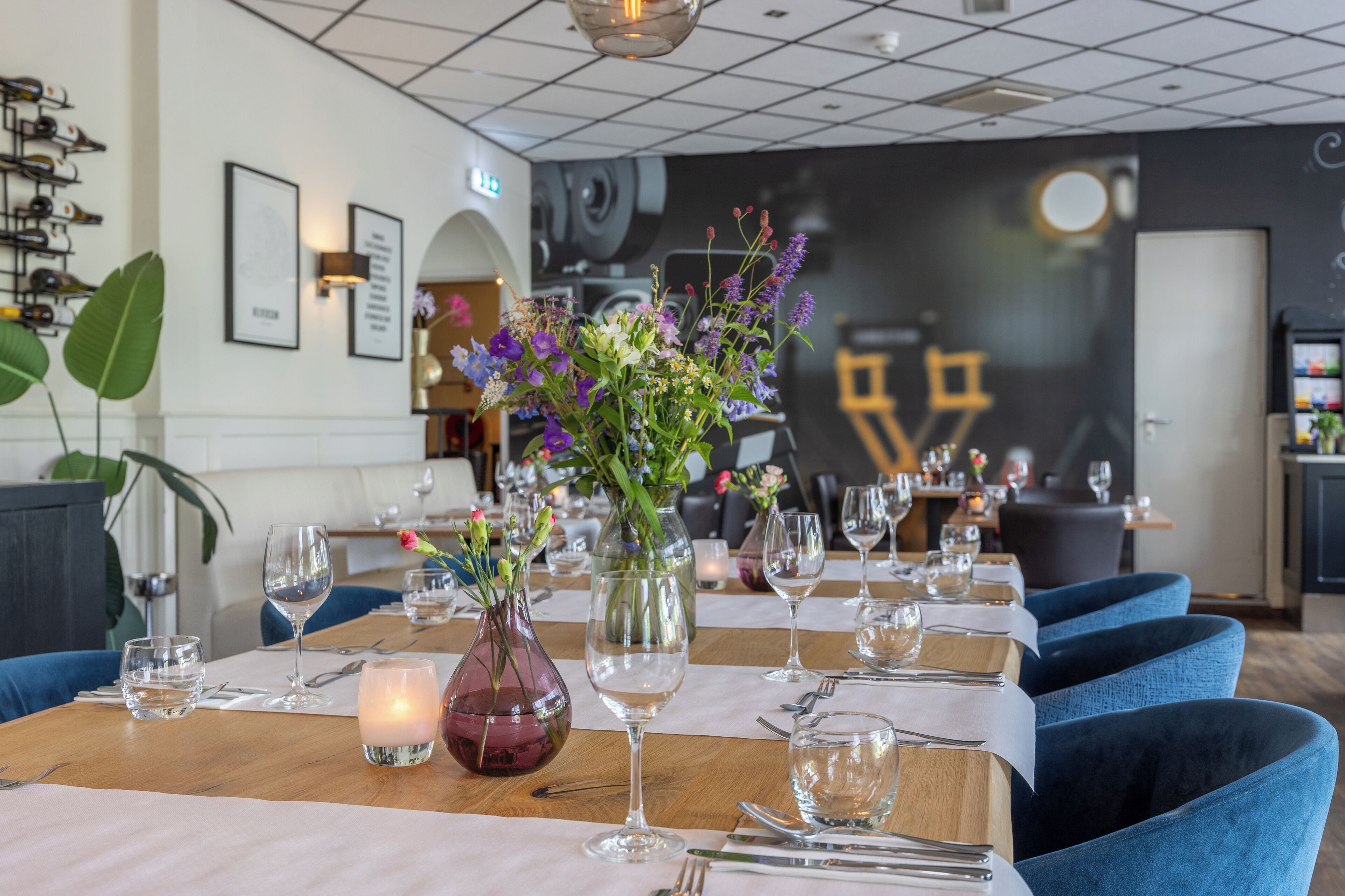 A restaurant with tables set for dining, featuring vases with flowers and candles.