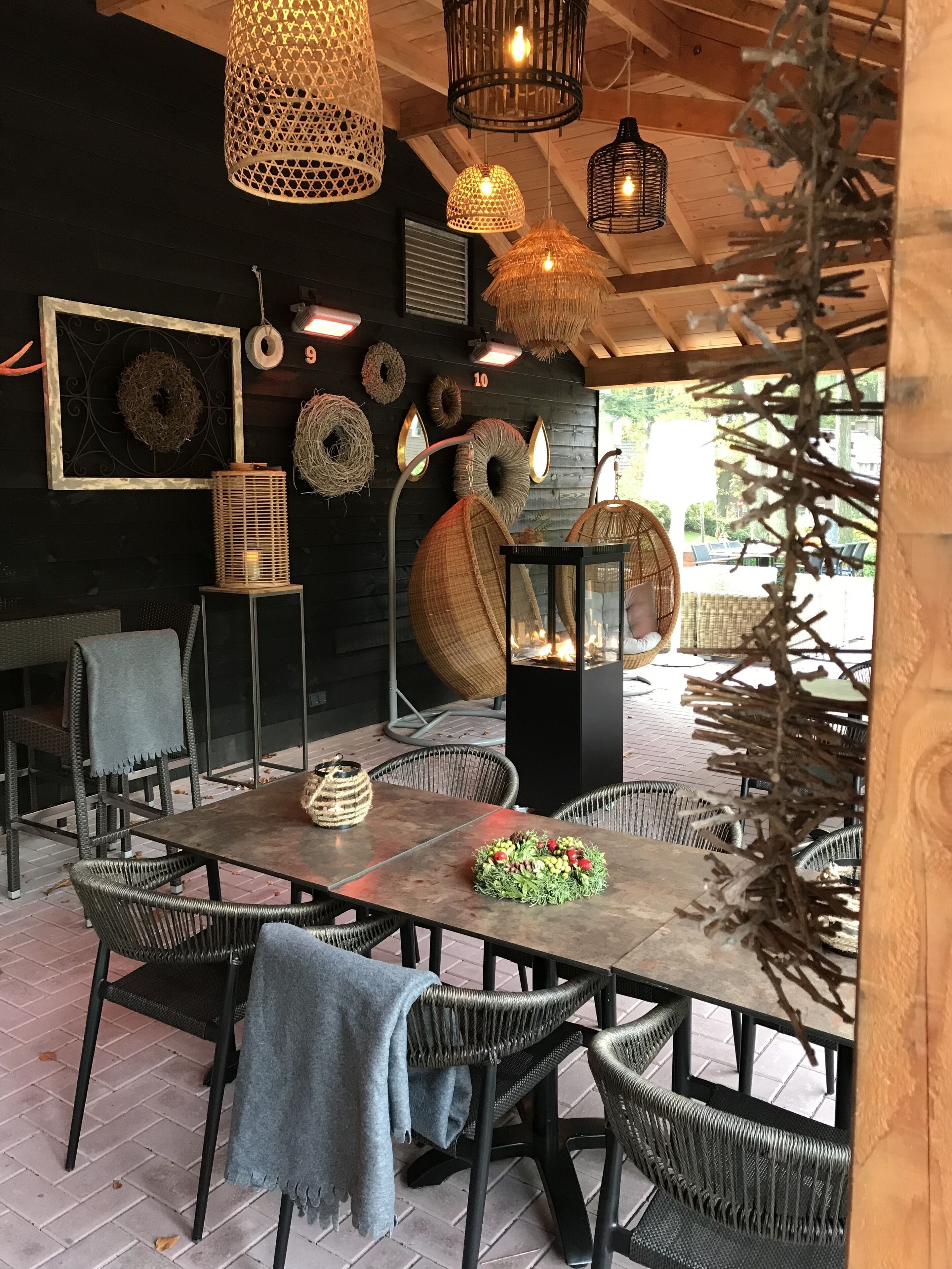 Een terras met buitenmeubilair van riet, hangende lampen en decoratieve wandversieringen.