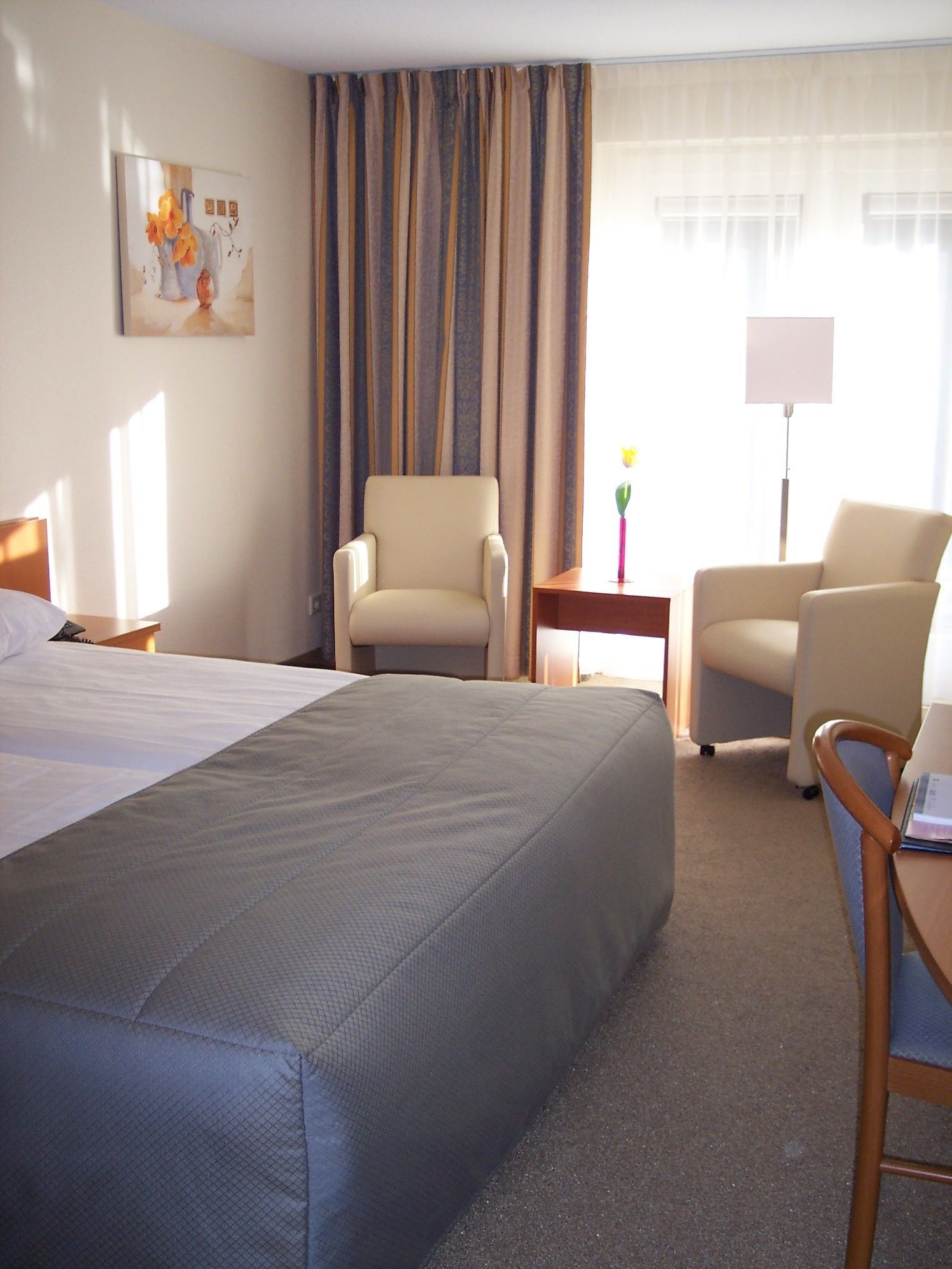 Une chambre d’hôtel avec un grand lit, deux fauteuils, une petite table et un tableau au mur.