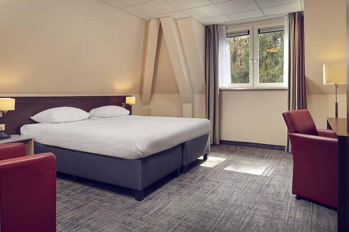 A hotel room with a large bed, a desk, a chair, and a window with curtains.
