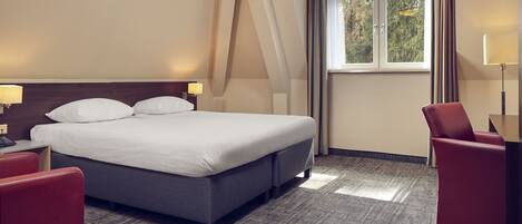 A hotel room with a large bed, a desk, a chair, and a window with curtains.