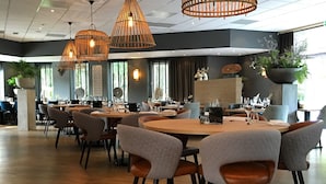 A modern dining area with round tables, grey upholstered chairs, and hanging wicker pendant lights. - Hotel De Werelt Garderen (Garderen)