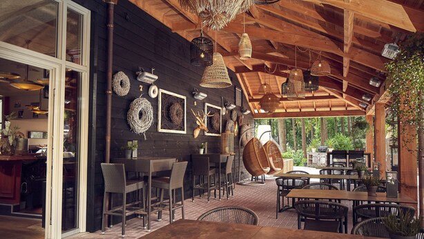 An outdoor dining area with wicker furniture, hanging wicker light fixtures, and a wooden ceiling. - Hotel De Werelt Garderen (Garderen)