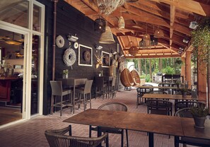 Un espacio exterior para comer con mobiliario de mimbre, lámparas colgantes de mimbre y techo de madera.
