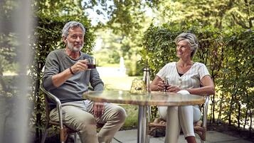 Dos personas sentadas en una mesa redonda al aire libre, rodeadas de vegetación.