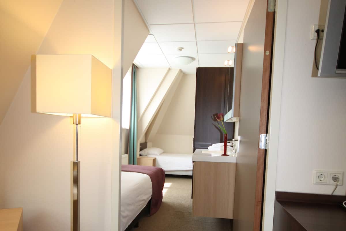 A hotel room with a bed, bedside table, lamp, and a small desk with a mirror.