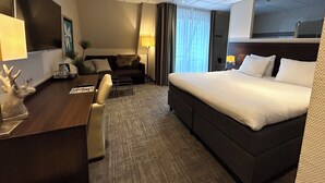 A hotel room with a bed, a desk with a lamp, a sofa, and a TV. - Hotel De Werelt Garderen (Garderen)
