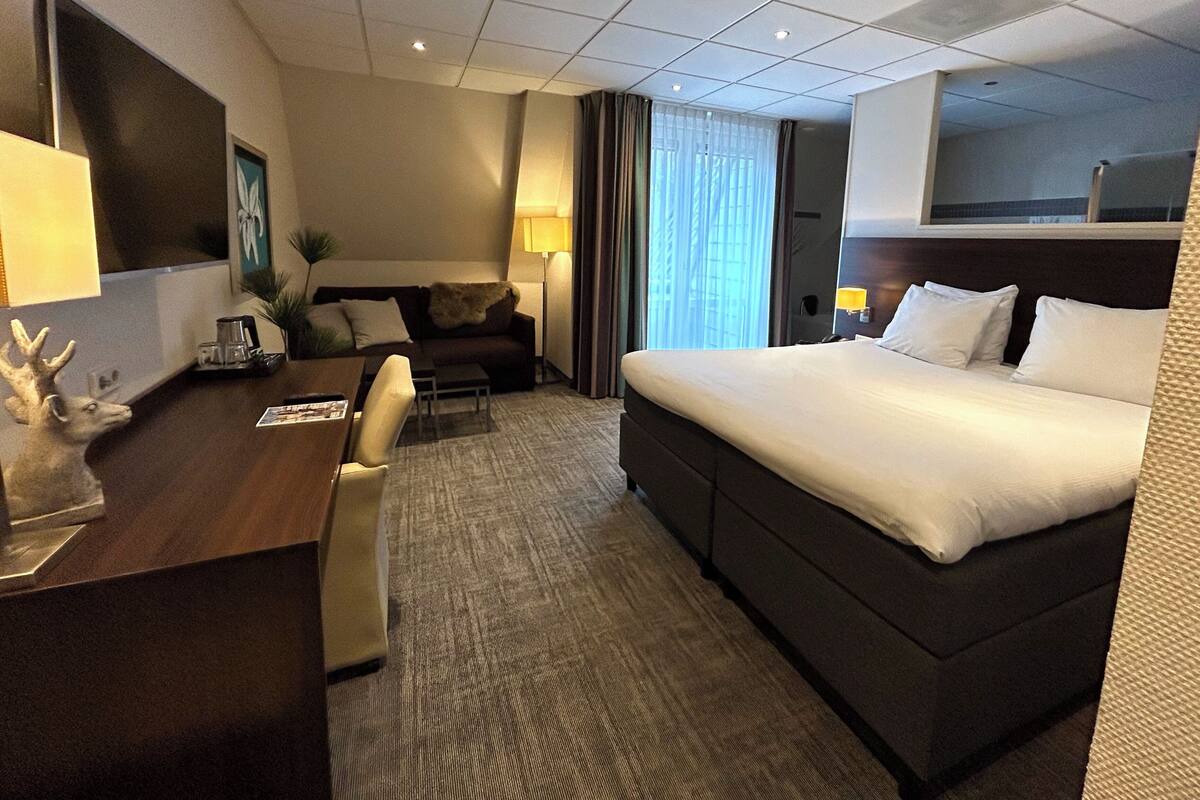 A hotel room with a bed, a desk with a lamp, a sofa, and a TV.